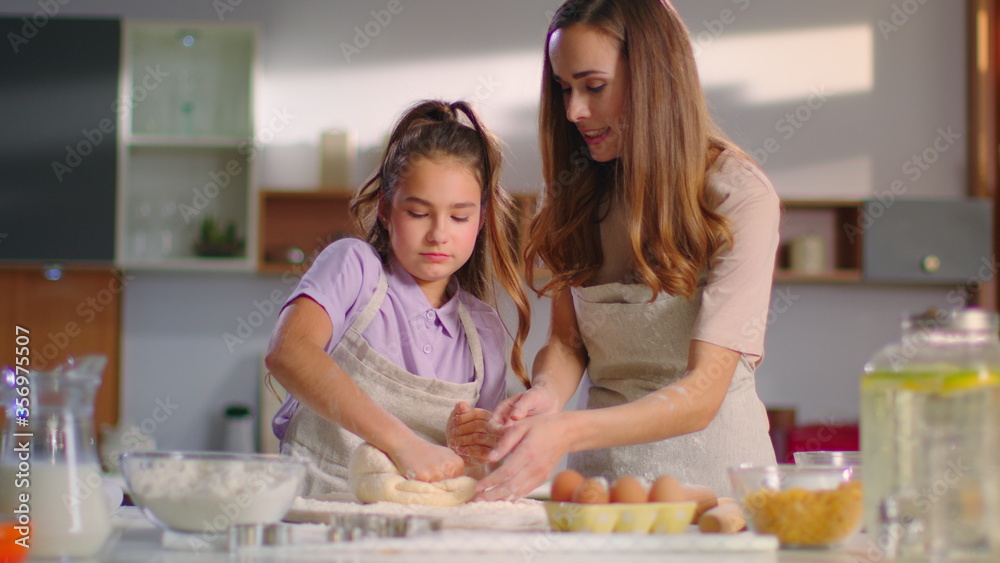 Mother teaching daughter to knead dough for cookies on kitchen in slow motion