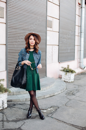 Fashionable brunette in brown hat, jeans jacket and choker on neck posing at street,looking at camera. Confident stylish woman with handbag, after beauty salon and shopping. Street swag style. © Вячеслав Косько