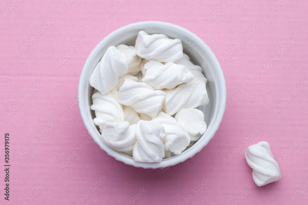 White marshmallows in a white porcelain plate on a pink background. View from above White marshmallows in a white porcelain plate on a pink background. View from above
