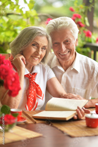 Portrait of happy senior couple reading book while drinking coffee