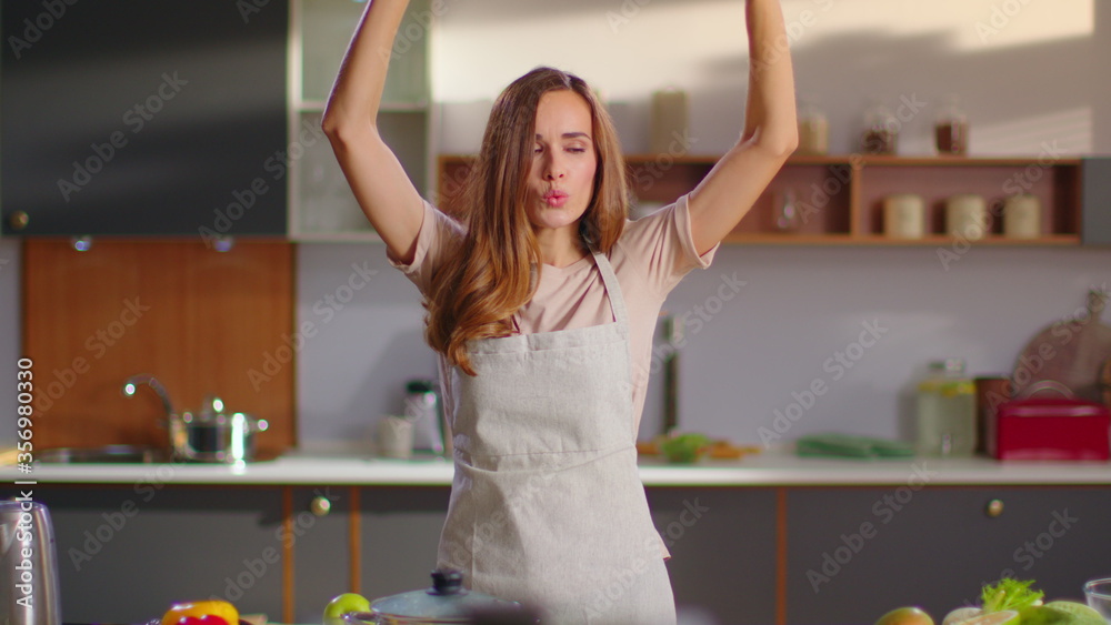 Obraz premium Cheerful housewife in apron cooking soup on kitchen. Woman dancing at home