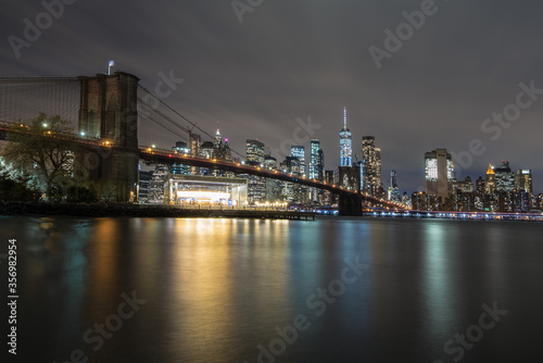 New York City skyline behind the Brooklyn Bridge at night. 