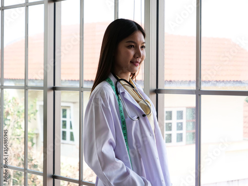 Asian female nutritionist stands to relax and enjoy the view at the window.