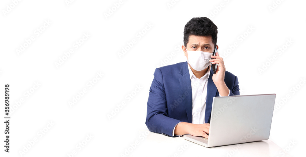 Business Asian man wearing a mask holding mobile phone That has The computer page in front of. on white background in studio With copy space,Concept work from home covid-19. Business Asian man wearing a mask holding mobile phone That has The computer page in front of. on white background in studio With copy space,Concept work from home covid-19.