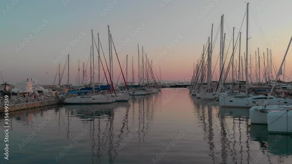 Aerial drone bird's eye view of marina with docked yachts in sunset time. Camera moves forward between boats. Aerial drone bird's eye view of marina with docked yachts in sunset time. Camera moves forward between boats.