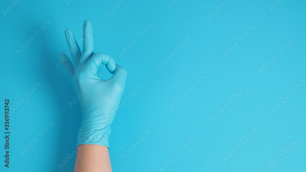 Male 's hand with doctor glove is doing a ok hand sign on blue background. Male 's hand with doctor glove is doing a ok hand sign on blue background.