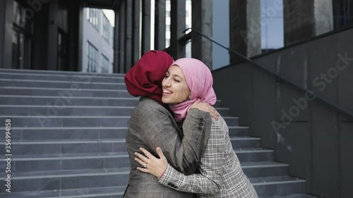 Two young Muslim women wearing hijab headscarf greet each other, hug eash other, modern lifestyle, technology, business discussions, leisure time. photo