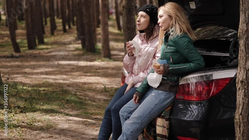 Two girlfriends on picnic in the woods near the trunk of the car