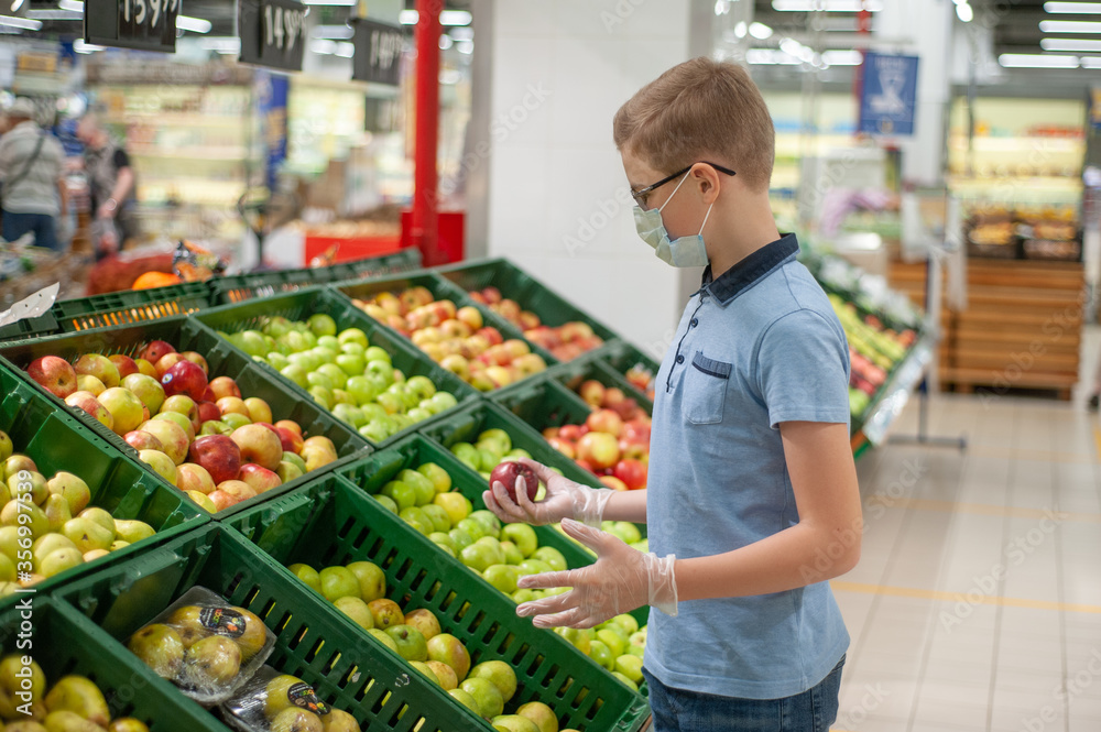 Teenager in the supermarket wearing a mask and gloves. He chooses fruit.