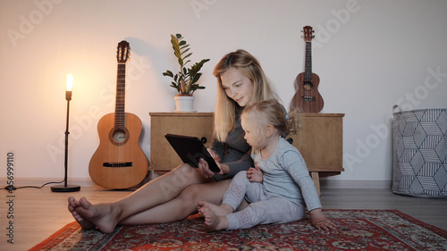 Young mother and daughter sitting on floor and talking by video link