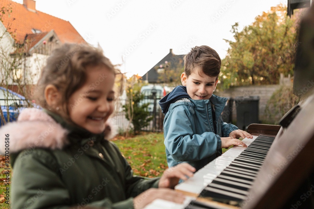 Smiling girl playing piano with brother in backyard Smiling girl playing piano with brother in backyard