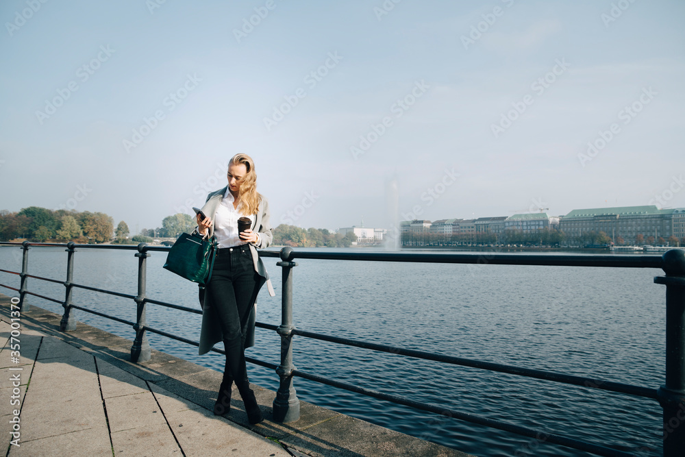 Full length of entrepreneur using mobile phone while standing against sea in city Full length of entrepreneur using mobile phone while standing against sea in city