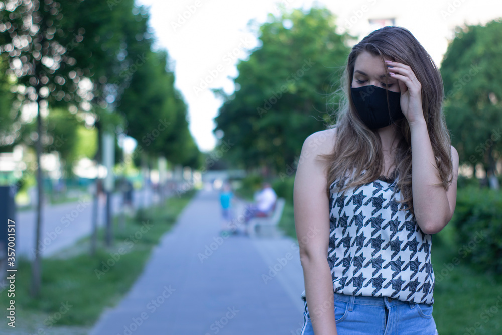 Pretty young blonde woman in medical black face mask. Wearing a t-shirt and jeans shorts. in a park. modern reality. covid-19 concept. copy space. High quality photo Pretty young blonde woman in medical black face mask. Wearing a t-shirt and jeans shorts. in a park. modern reality. covid-19 concept. copy space. High quality photo