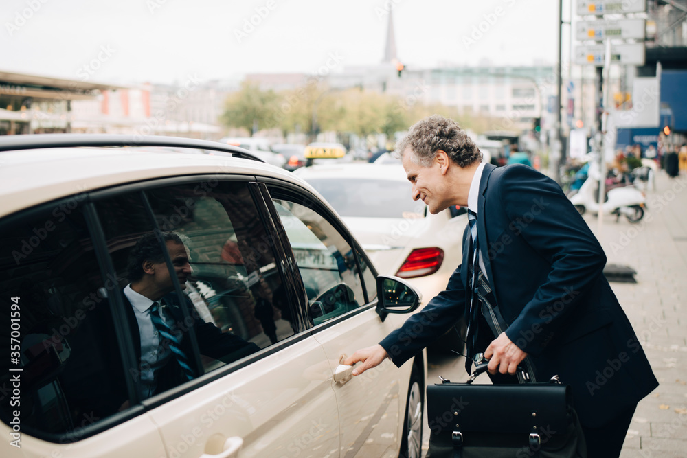 Side view of mature businessman holding taxi door in city Side view of mature businessman holding taxi door in city