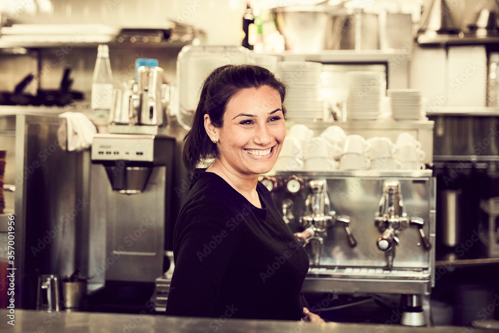 Side view of smiling owner looking away while standing at checkout counter in cafe Side view of smiling owner looking away while standing at checkout counter in cafe