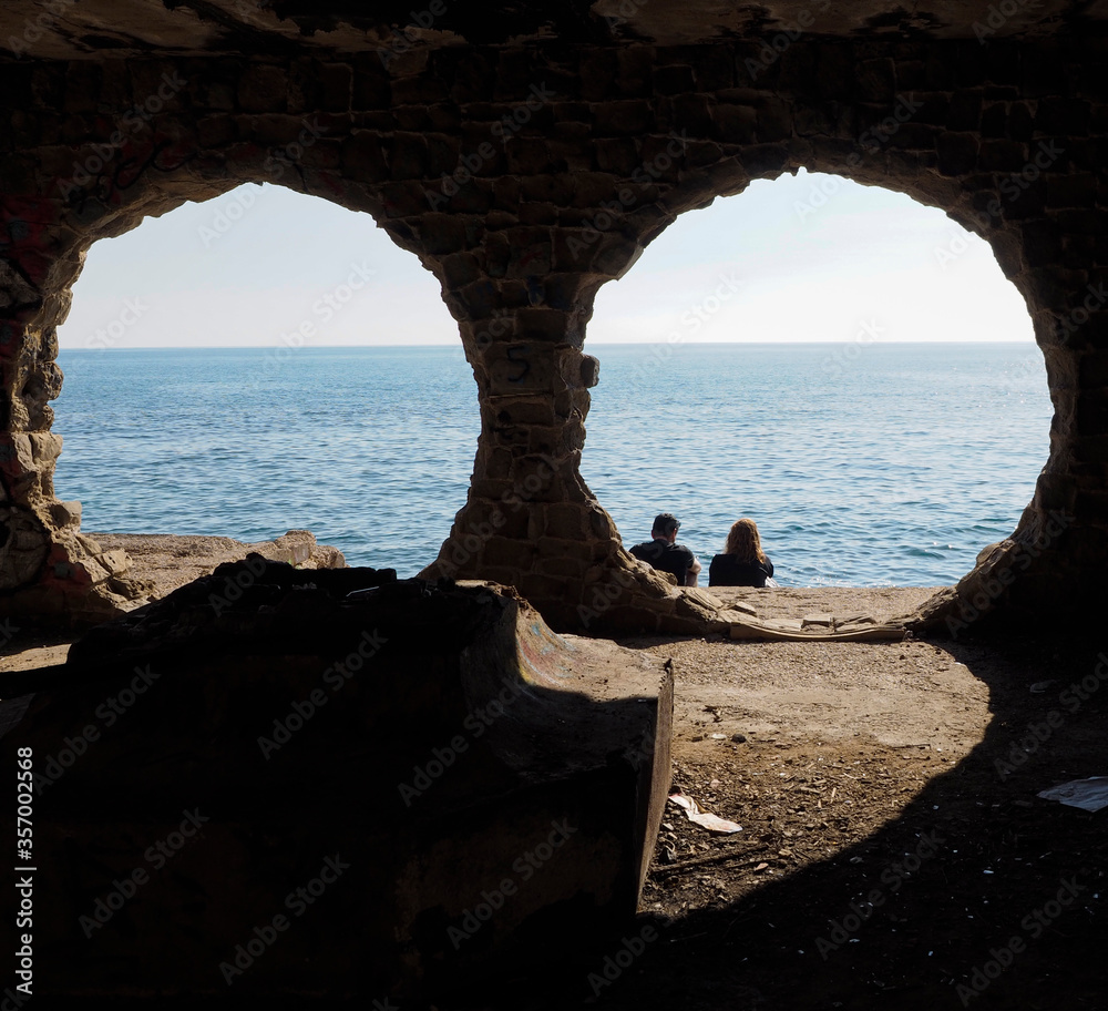 Pareja sentada mirando el mar junto a unas circunferencias de piedra
