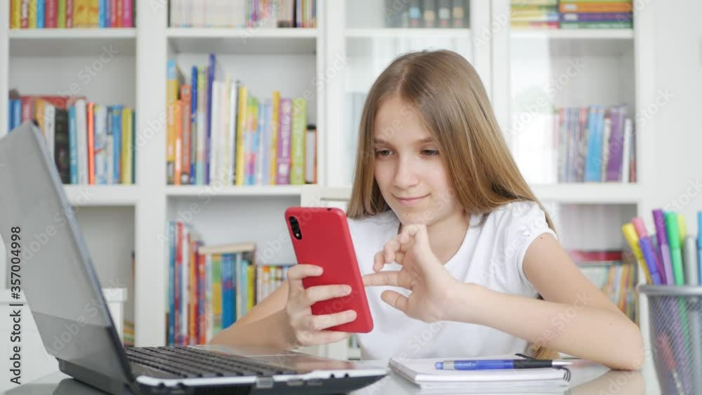 Kid Using Smartphone Studying in Video Conferencing, Child Learning, Writing in Library, Schoolgirl Chatting with Teacher at Home in Coronavirus Pandemic Crisis, Homeschooling, Online Education Kid Using Smartphone Studying in Video Conferencing, Child Learning, Writing in Library, Schoolgirl Chatting with Teacher at Home in Coronavirus Pandemic Crisis, Homeschooling, Online Education