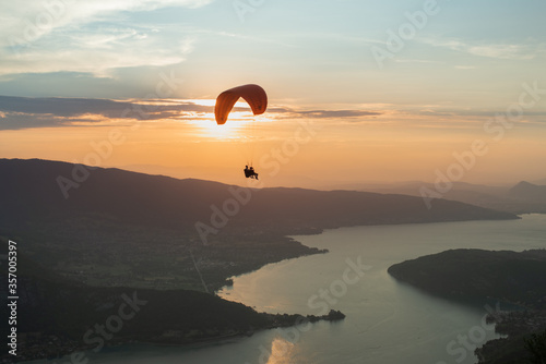 tandem paraglider flying over a beautiful winding lake at sunset.