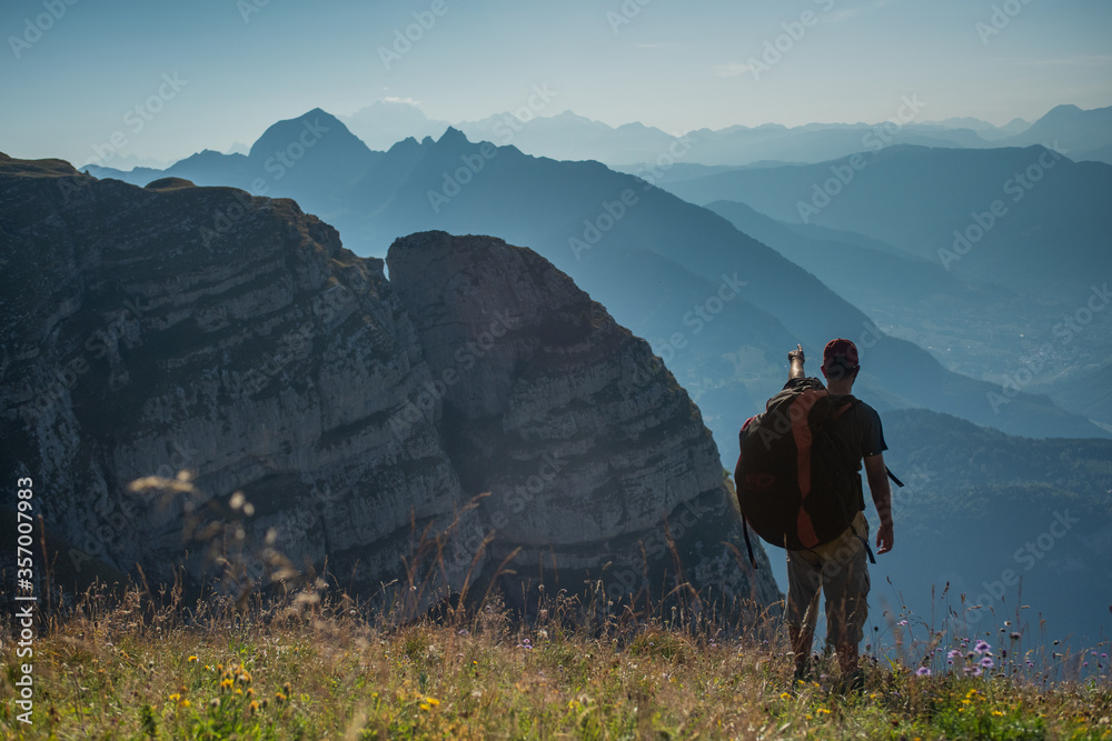 young man standing on a mountain pointing down to the valley in the distant horizon.