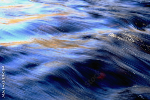 abstract image of dark blue flowing water with orange reflections of autumn coloured tree