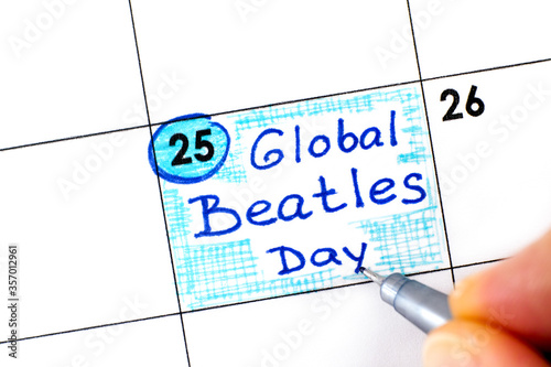 Woman fingers with pen writing reminder Global Beatles Day in calendar.