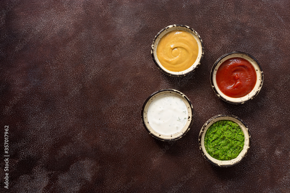 Collection of various sauces in the bowl: tomato, pesto, creamy with greens and mustard on a dark rustic background. Top view, copy space. Collection of various sauces in the bowl: tomato, pesto, creamy with greens and mustard on a dark rustic background. Top view, copy space.
