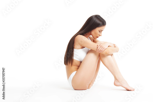 Slim young woman sits in underwear on white background