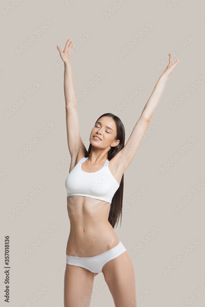 Slim young woman in underwear stretches and shows tender smooth armpit skin on beige background