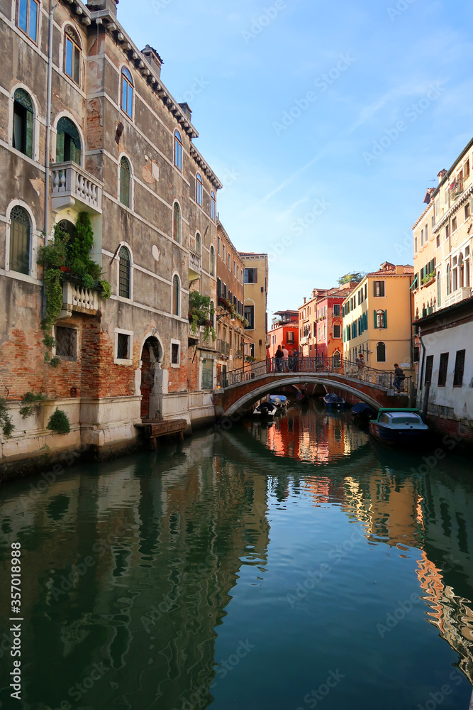 Beautiful view of a canal between colorful stone buildings of Venice , Italy. There is a nice reflection of the street on the river.
