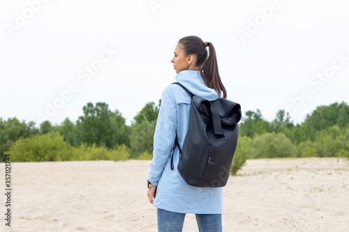 Young woman in a blue jacket with a backpack travels around outdoors. Hiking on trail at nature.