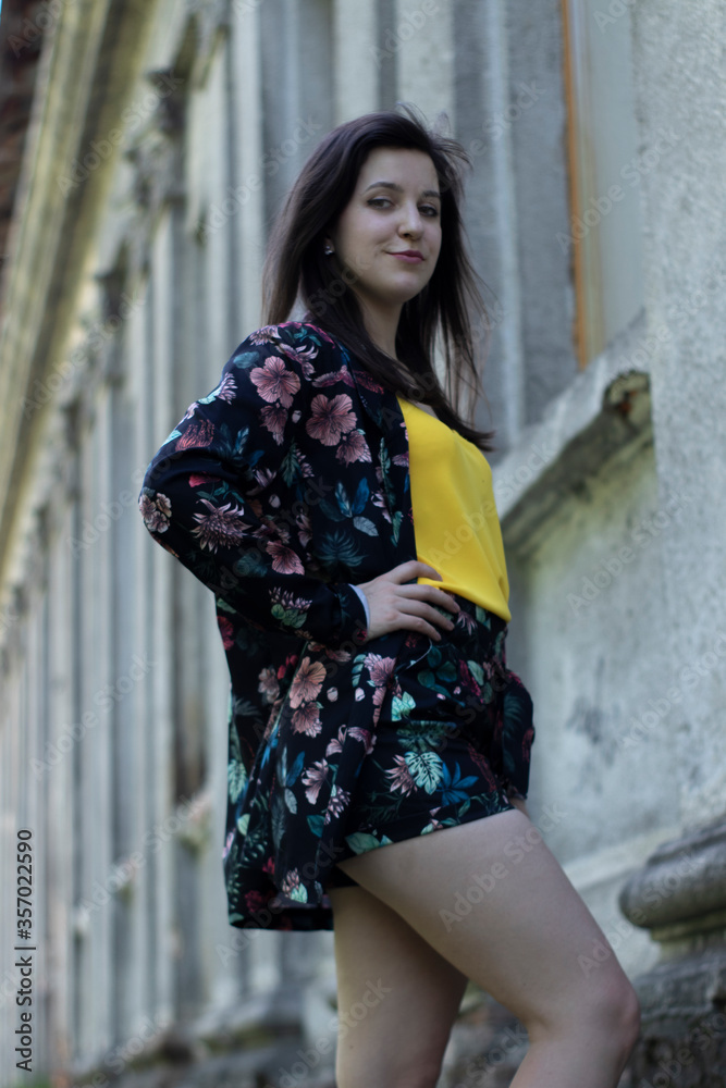 Attractive young brunette woman in yellow t-shirt and flowery shorts costume. old building background. copy space. High quality photo Attractive young brunette woman in yellow t-shirt and flowery shorts costume. old building background. copy space. High quality photo
