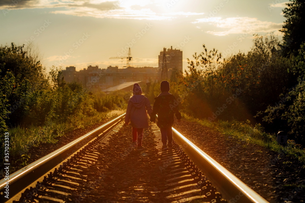 little children walk hand in hand on the railroad towards the setting sun