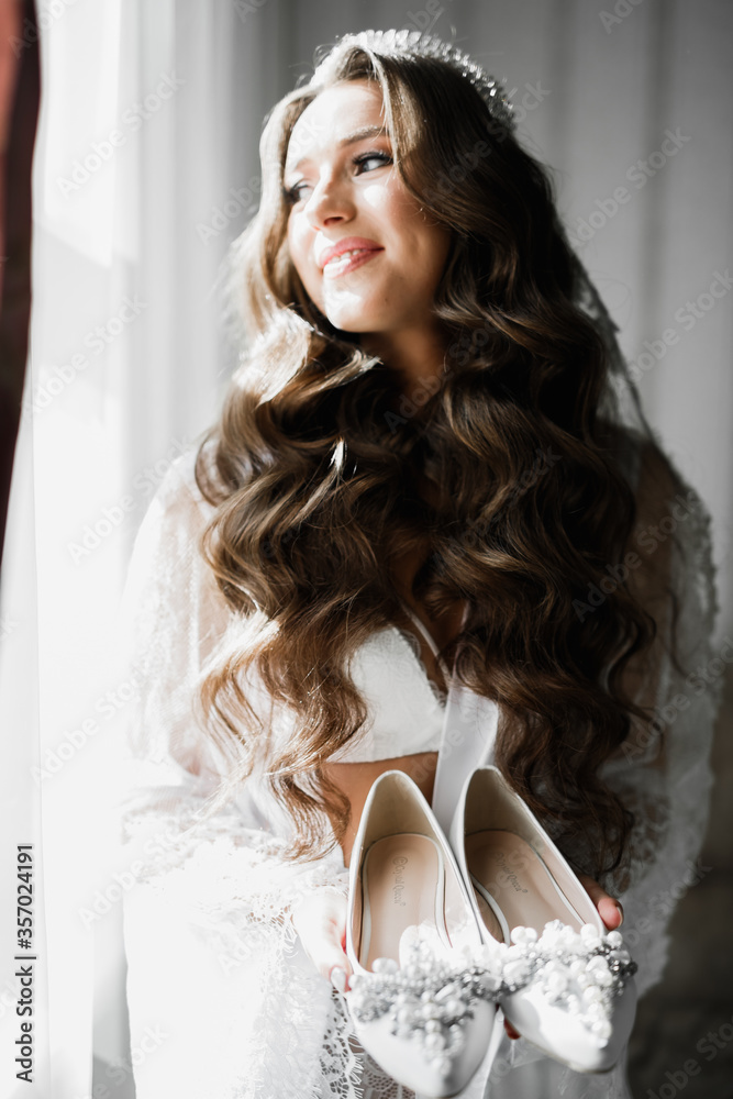 Beautiful luxury bride in elegant white dress holds wedding shoes in the hands