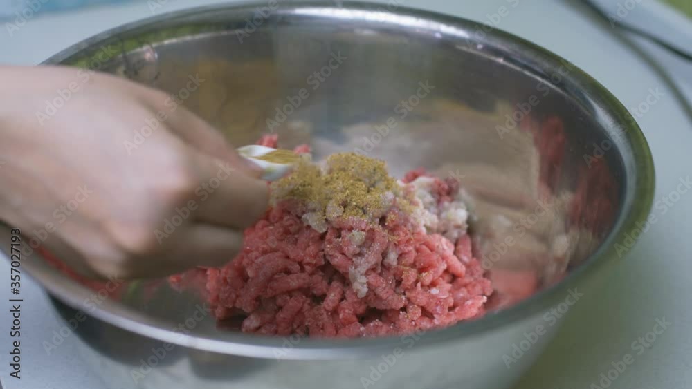 The process of cooking cutlets. Woman hand seasoning stuffed meat in the metallic bowl The process of cooking cutlets. Woman hand seasoning stuffed meat in the metallic bowl