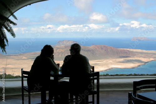 Silhuettes a couple of older people looking at a dream island throuth a cafe window
