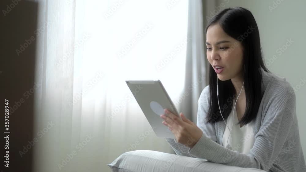 Work from home concept. Smiley asian woman wear headphone video conference calling on tablet talk by webcam in online chat. Slow Motion Full HD. Work from home concept. Smiley asian woman wear headphone video conference calling on tablet talk by webcam in online chat. Slow Motion Full HD.