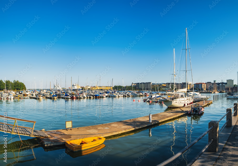 Scenic Finnish cityscape of Scandinavian Old Town pier with old boats and sailing ship in sea harbor on summer day. Katajanokka district is a famous tourist destination in Helsinki city, Finland