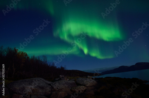mighty aurora borealis dancing on night sky over mountain and fjord landscape in late autumn in the arctic circle © Arcticphotoworks