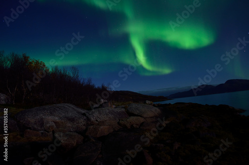 mighty aurora borealis dancing on night sky over mountain and fjord landscape in late autumn in the arctic circle © Arcticphotoworks