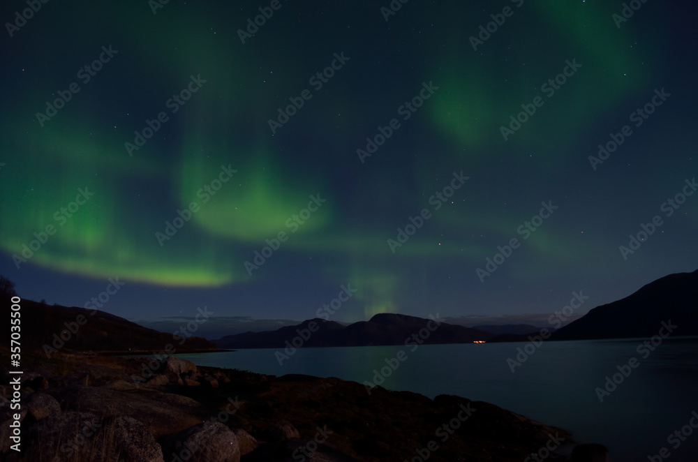 mighty aurora borealis dancing on night sky over mountain and fjord landscape in late autumn in the arctic circle