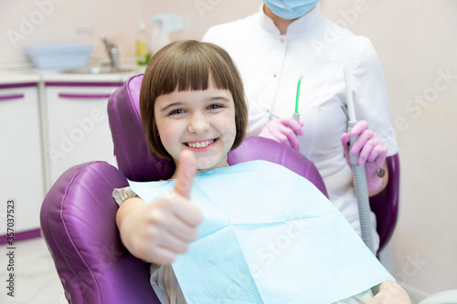 Little girl showing thumb-up approving pediatric dental service in modern clinic for children. 