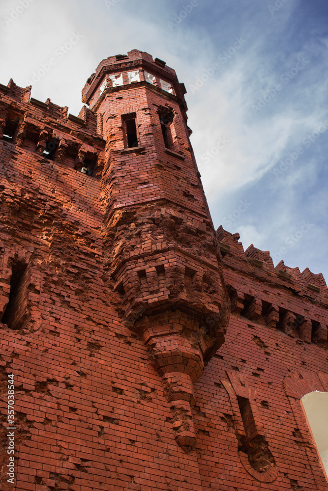 Abandoned medieval castle with red brick walls and tall tower against blue sky