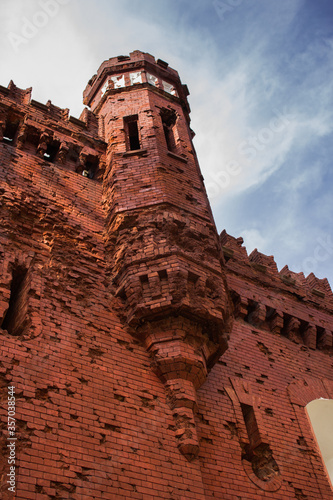 Abandoned medieval castle with red brick walls and tall tower against blue sky © Murloc