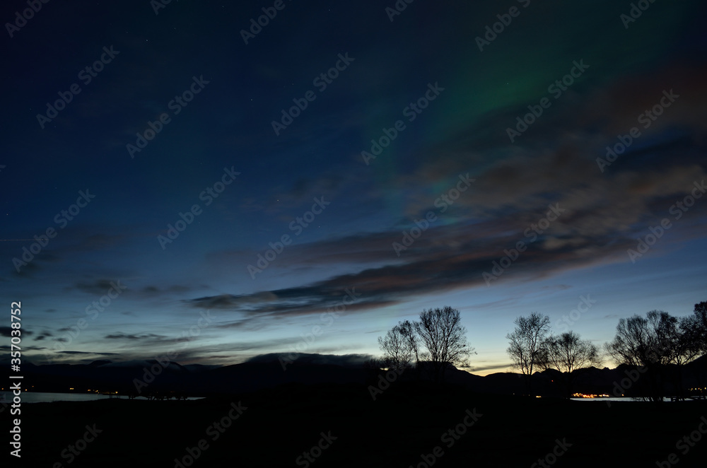 faint aurora borealis dancing over fjord and trees faint aurora borealis dancing over fjord and trees