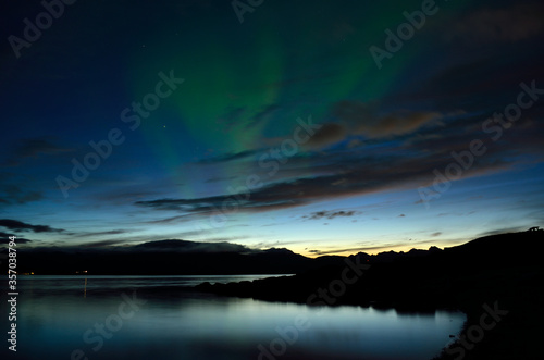 beautiful aurora borealis dancing over calm fjord and mountains
