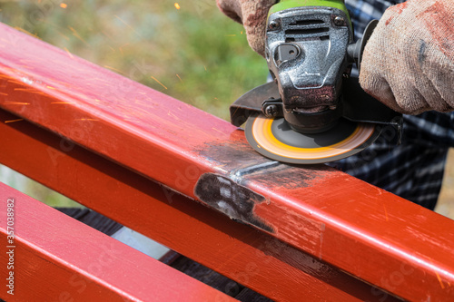 Worker cleans welding seam on steel closed profile using an electric wheel grinding machine