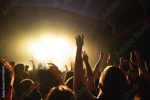 Obraz na płótnie hands of a dancing crowd at a rock concert of a cool band. silhouette of a musician on stage in a haze. music festival banner w salonie