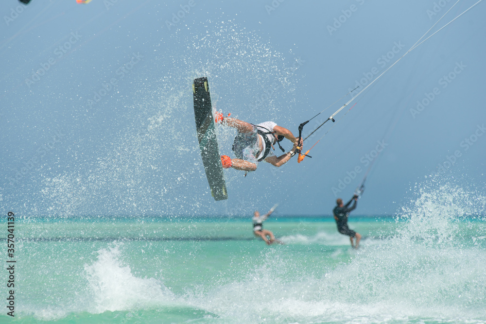 Naklejka premium kiter does a difficult trick on a background of transparent water and blue sky