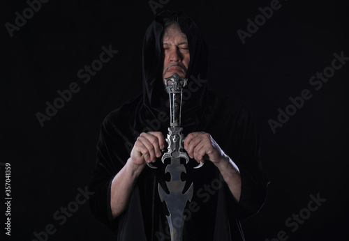 portrait of a medieval warrior in a hood with a sword on a black background
