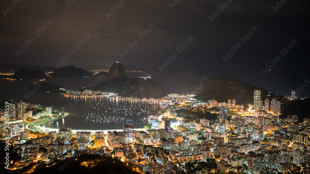 Night view over Rio de Janeiro looking at the bay and Sugarloaf Mountain with the city glowing.